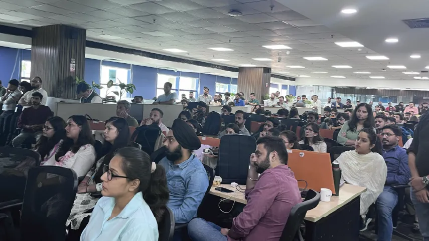 Large group of people seated and attentively listening in a modern office meeting or seminar room.