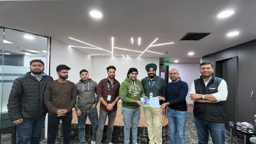 Group of eight men standing indoors in an office setting, two men in the center holding a certificate and smiling.