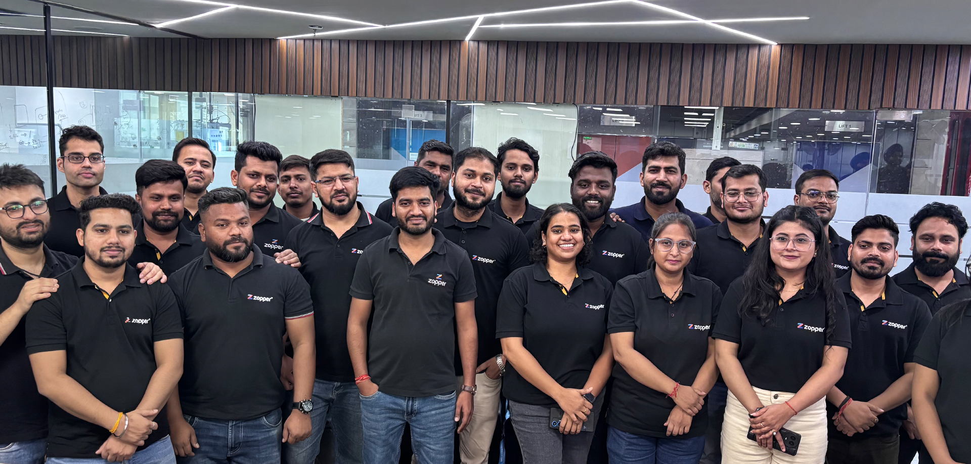 Group of people wearing black polo shirts with the Zopper logo standing together in an office setting.