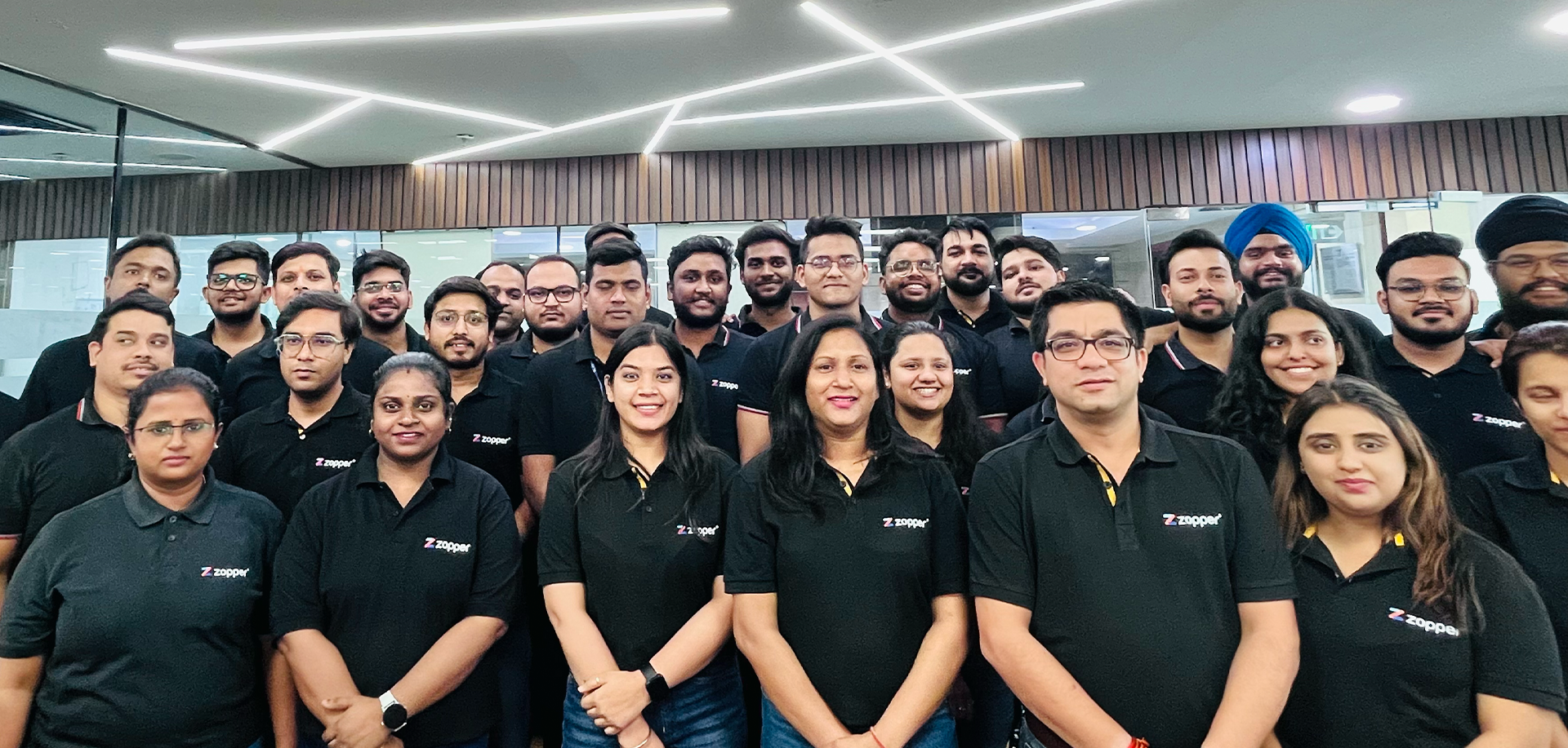 Group photo of diverse office team wearing matching black Zopper polo shirts in a modern office setting.