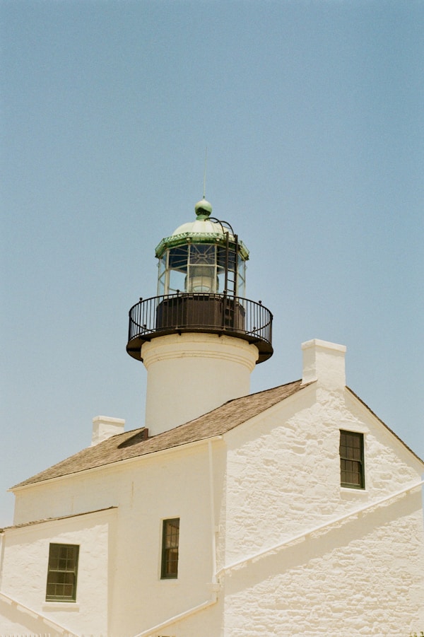 A white lighthouse shines brightly under a blue sky.