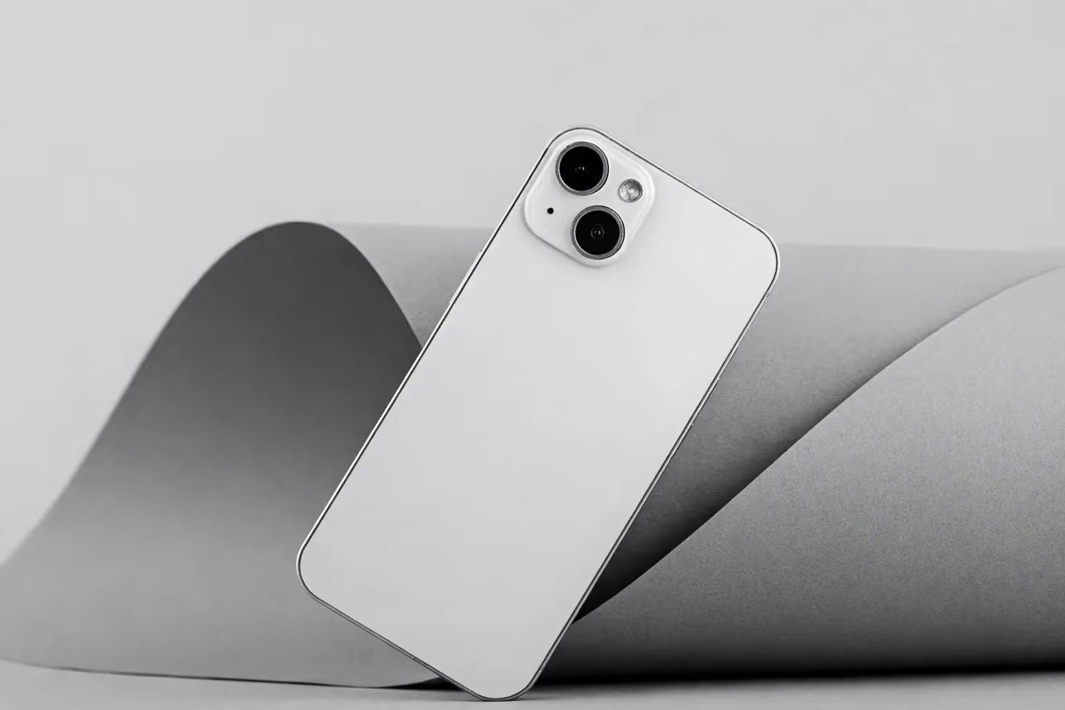 Czarno-białe zdjęcie smartfona opartego o szary, zwinięty papier w minimalistycznym stylu