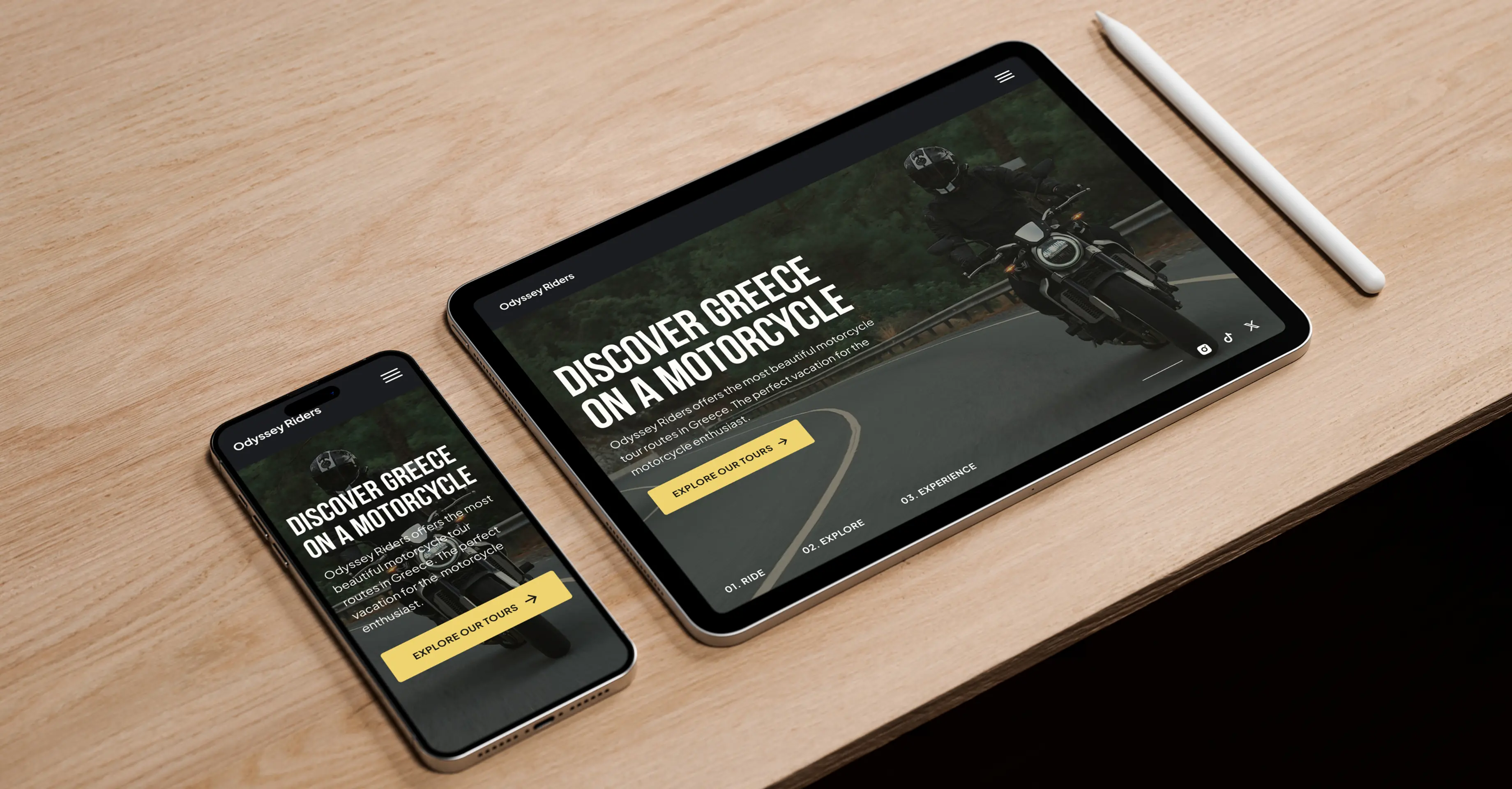 A tablet and mobile lying on a wooden desk with a digital pen next to the tablet. The devices each show a screenshot of the hero section of the Odyssey Riders website, each adapted to the specific viewport. The hero section features a heading titled “Discover Greece on a motorcycle”. Below is a short paragraph with the text “Odyssey Riders offers the most beautiful motorcycle tour routes in Greece. The perfect vacation for the motorcycle enthusiast”. Below the paragraph is a call to action button. The section features a background image showing a motorcyclist riding his bike on a country road in the forest.
