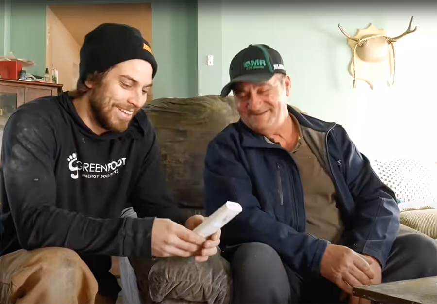 two men sitting on a couch looking at a wii remote