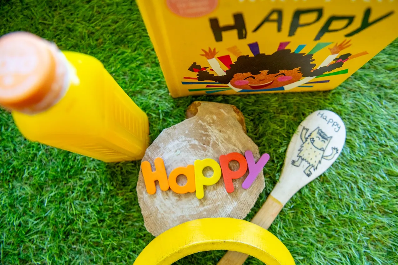 A "Happy" book, juice, and toys on grass, ideal for a nursery website showcasing a cheerful and playful learning environment.