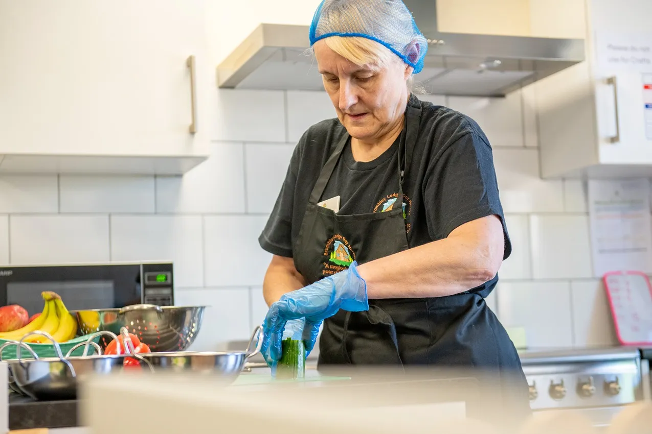 Nursery chef preparing healthy snacks. Woman in apron and gloves cuts cucumber for kids' meals at Brambley Lodge Day Nursery.