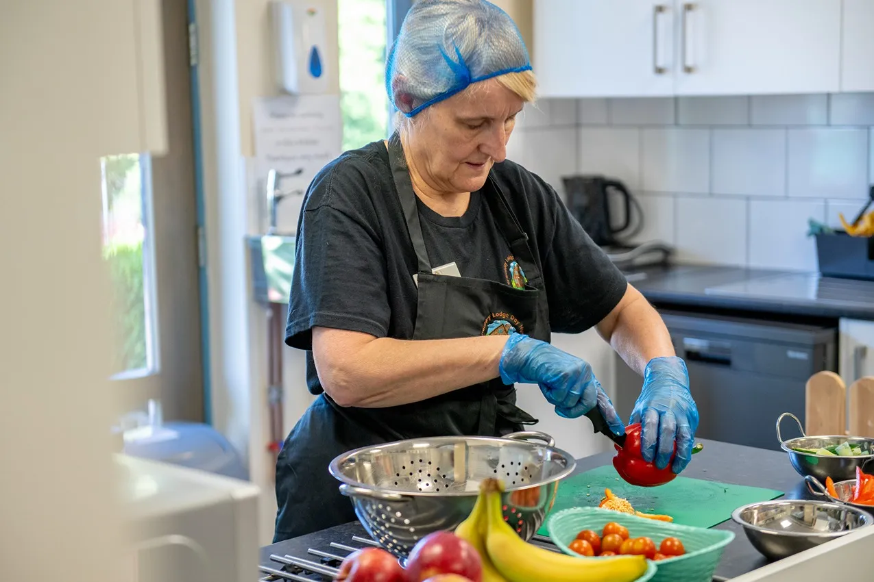 A nursery cook in a hair net and gloves prepares healthy food by chopping vegetables.