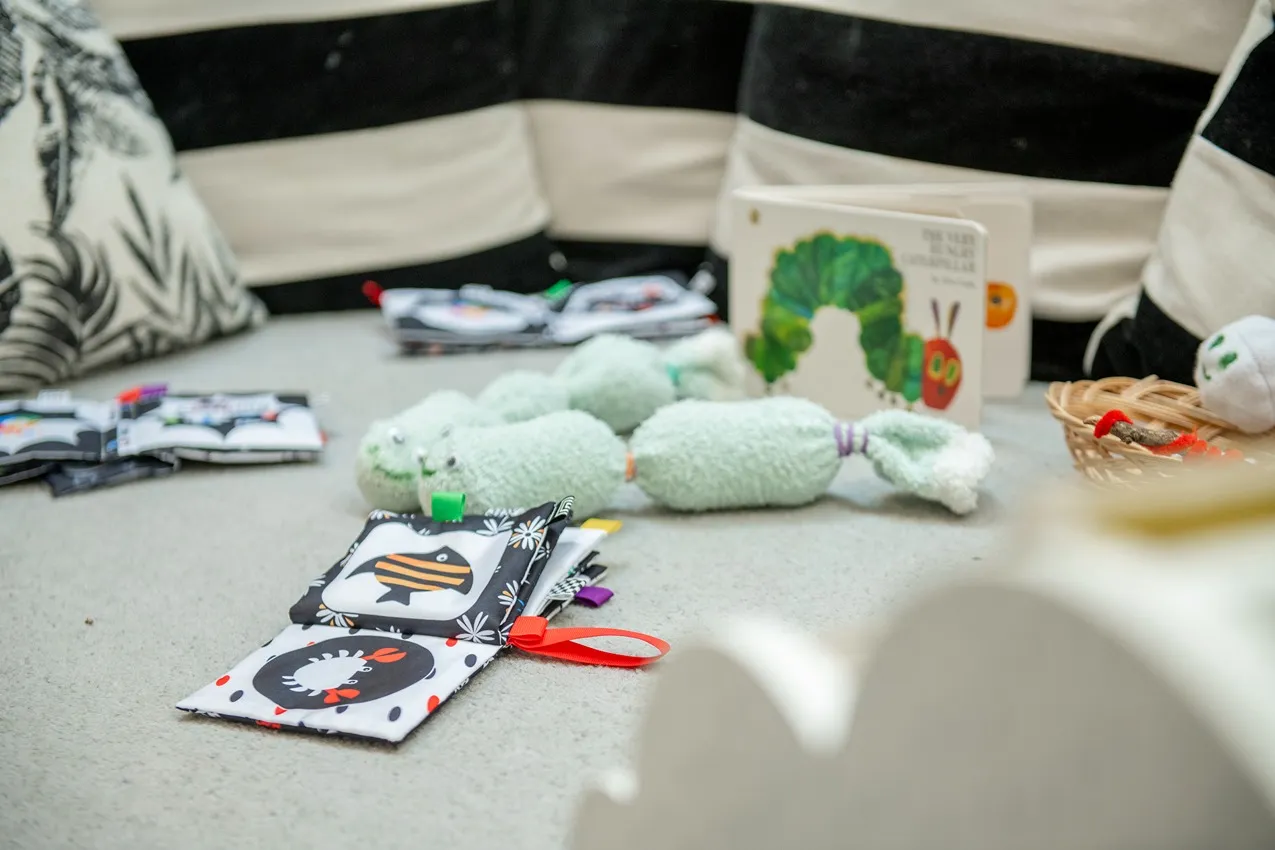 Baby nursery toys and books on the floor. Includes a soft book, caterpillar toy, and "The Very Hungry Caterpillar" book.