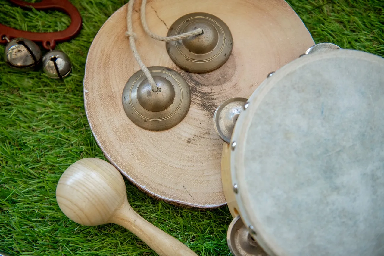 Nursery musical instruments: tambourine, cymbals, maraca, and bells on green grass.