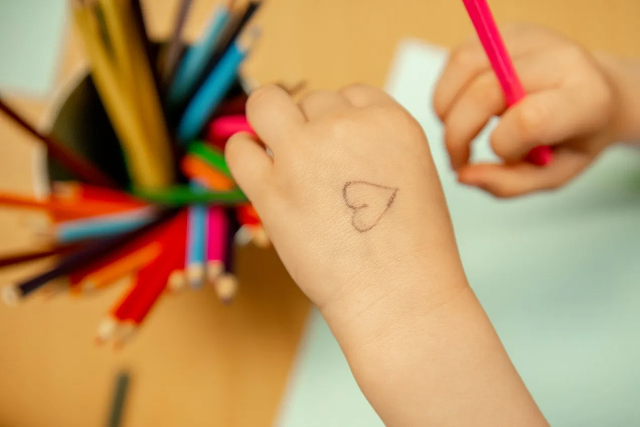 Child's hand with heart drawing, colorful pencils. Nursery art activity, creative learning.