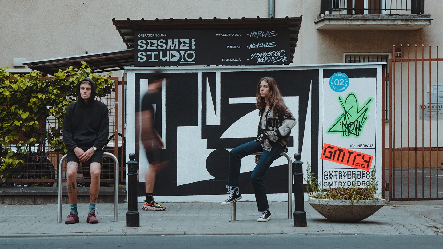 Dawid i Alicja z Sesme Studio siedzą przy muralu z logotypem studia na miejskim tle – główne zdjęcie na stronie sesmestudio.com przedstawiające zespół kreatywny w przestrzeni publicznej z elementami street artu