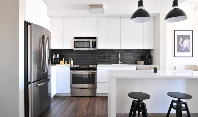 A kitchen with a stove, refrigerator, and two stools.