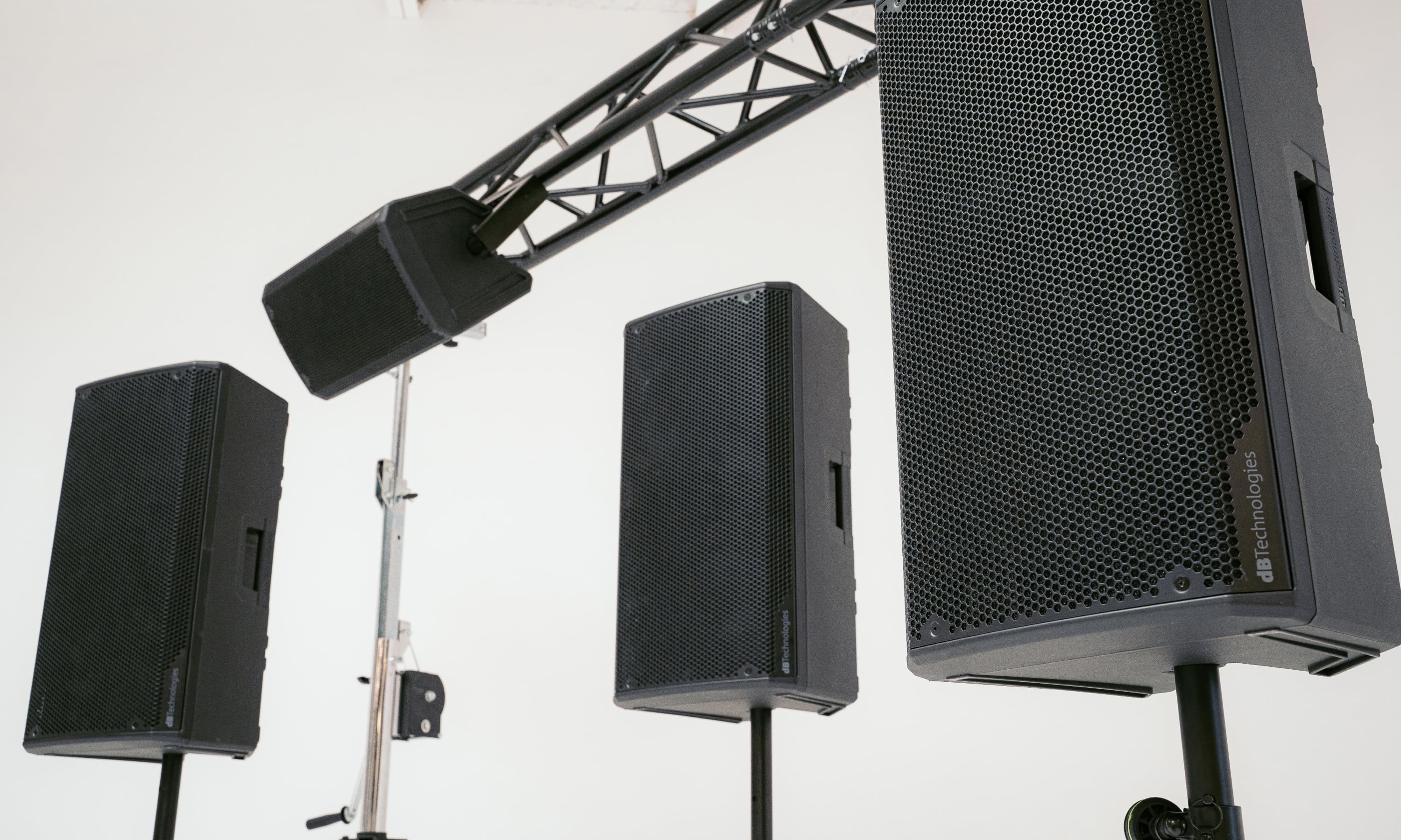 Three large black dB Technologies speakers mounted on stands in a white studio space.