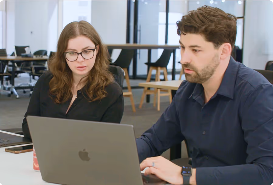 Two colleagues, a woman and a man, working together on a laptop in a modern office setting.