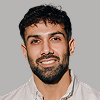 Headshot of a young man with dark curly hair, beard, and mustache, smiling and wearing a light-colored shirt against a gray background.