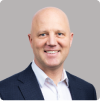 Smiling bald man in a navy suit jacket and white shirt against a gray background.