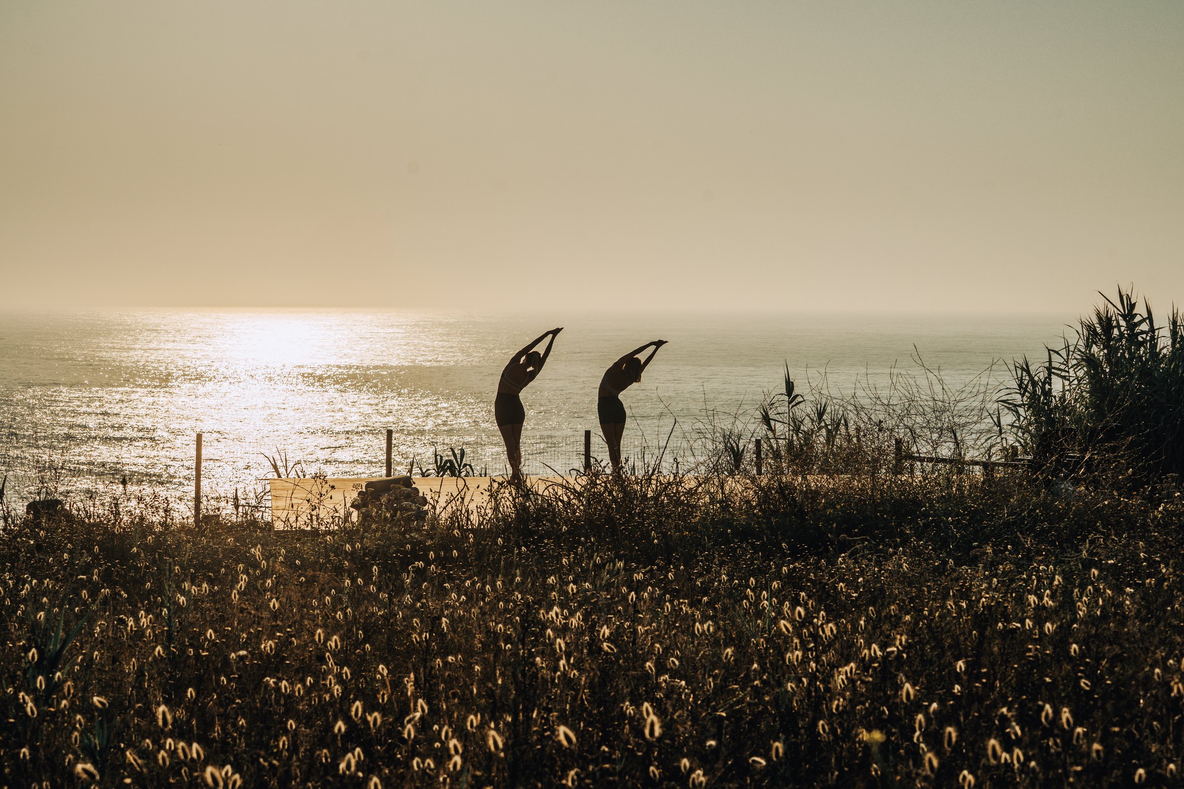 Two figures stretching against the sunset over the ocean