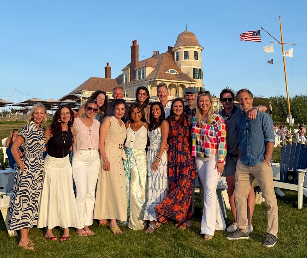 The group standing together on the lawn of a shingled waterfront house