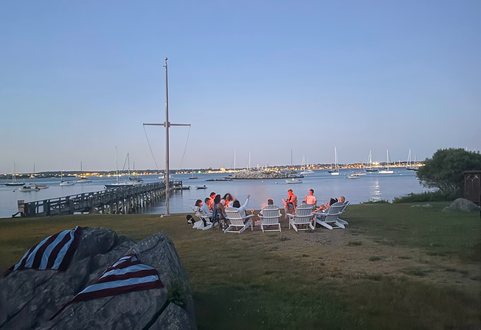 Group gathered on the shoreline at dusk beside a moored sailing boat