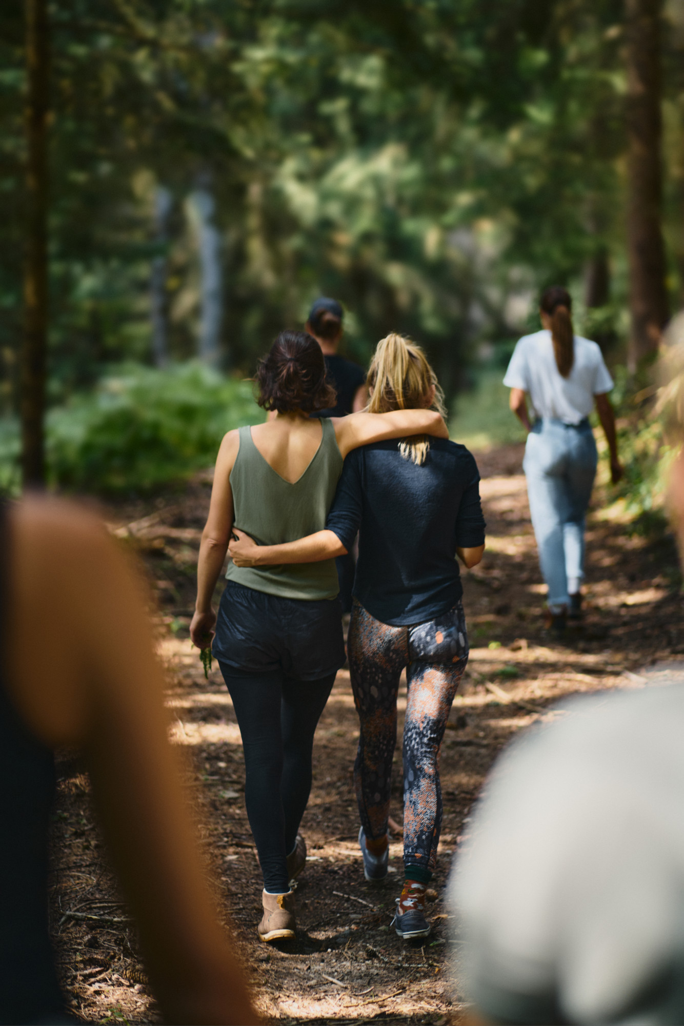 Two participants walking arm in arm along a wooded path