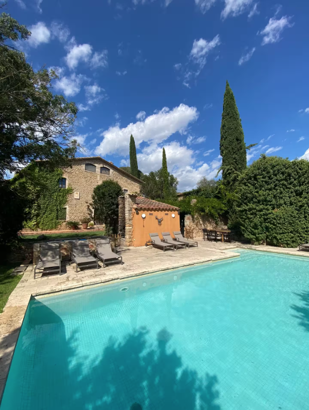 The pool and stone farmhouse under a bright blue sky