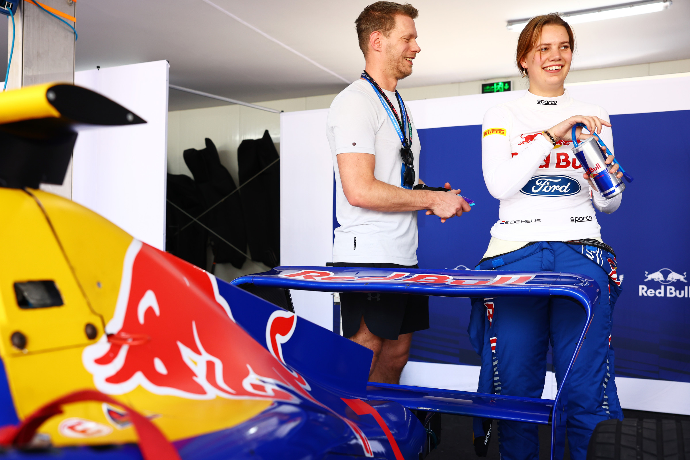 Two people talking beside a race car at a media event