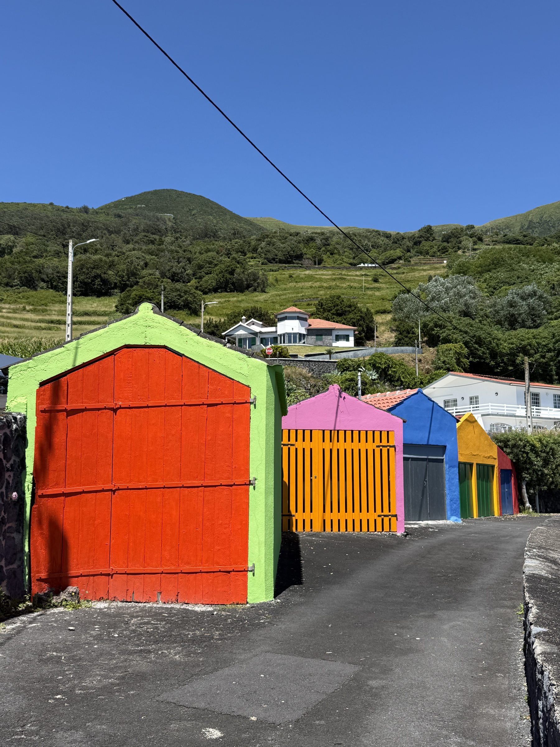 Brightly painted boat garages on a lane below green hills