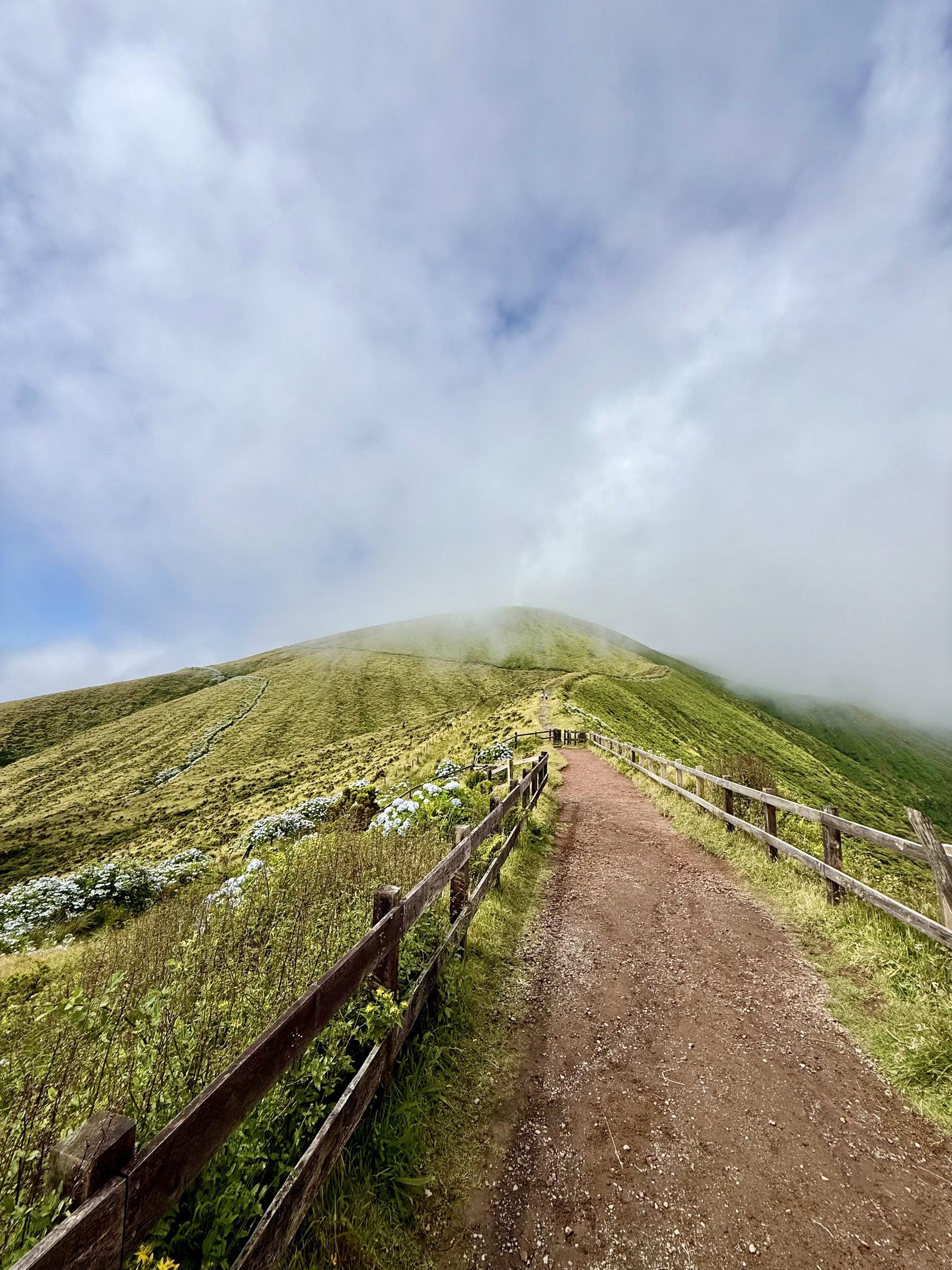 A fenced path climbing the caldera rim into low cloud
