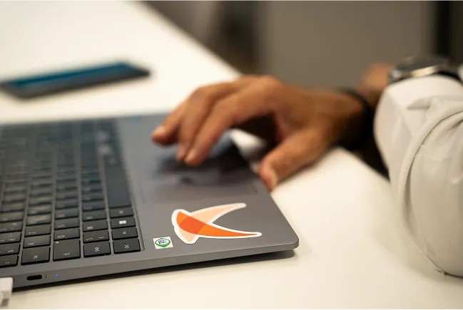 Main d’un homme posée sur un ordinateur portable gris avec un autocollant orange qui représente le logo BatiFire