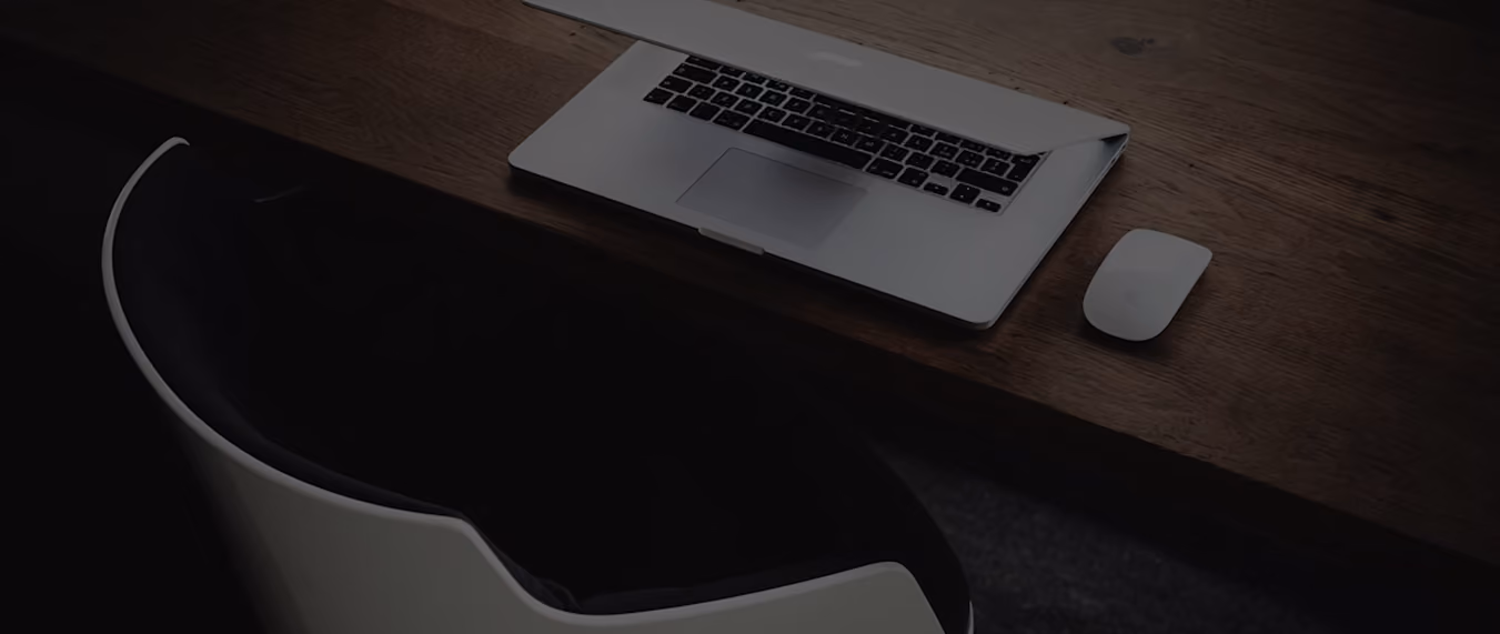 Ordinateur portable ouvert et souris blanche posés sur un bureau en bois, avec une chaise noire et blanche à proximité.