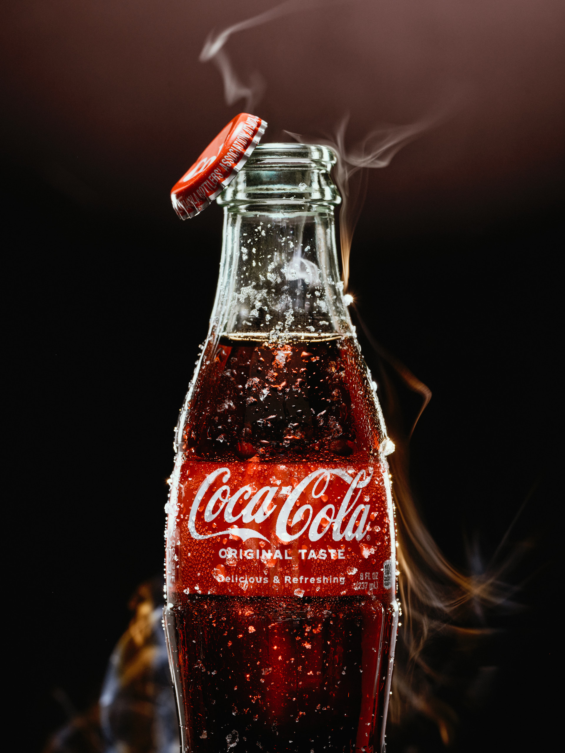 Classic glass Coca-Cola bottle with condensation, placed on a neutral surface in soft natural light, highlighting food and beverage photography.