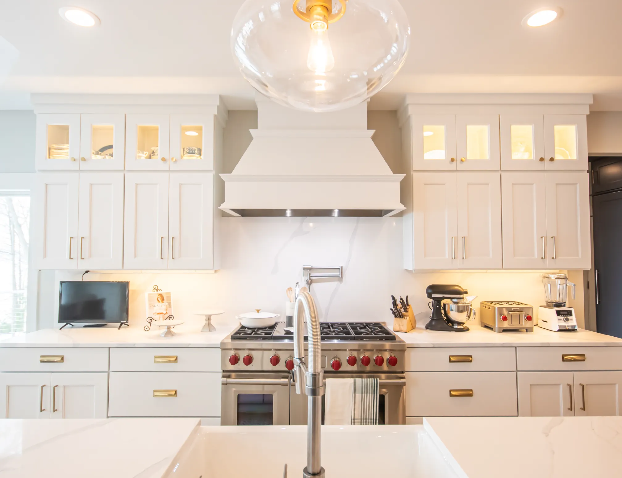 Modern white kitchen with stainless steel stove, white cabinetry, and countertop appliances including a mixer and toaster.