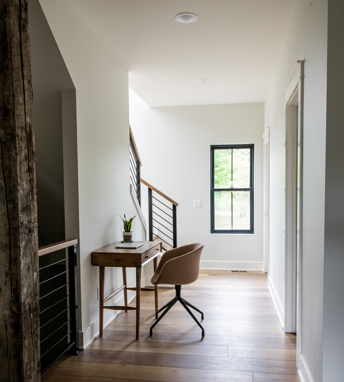 Minimalist home workspace with wooden desk, potted plant, modern chair, and window showing greenery.