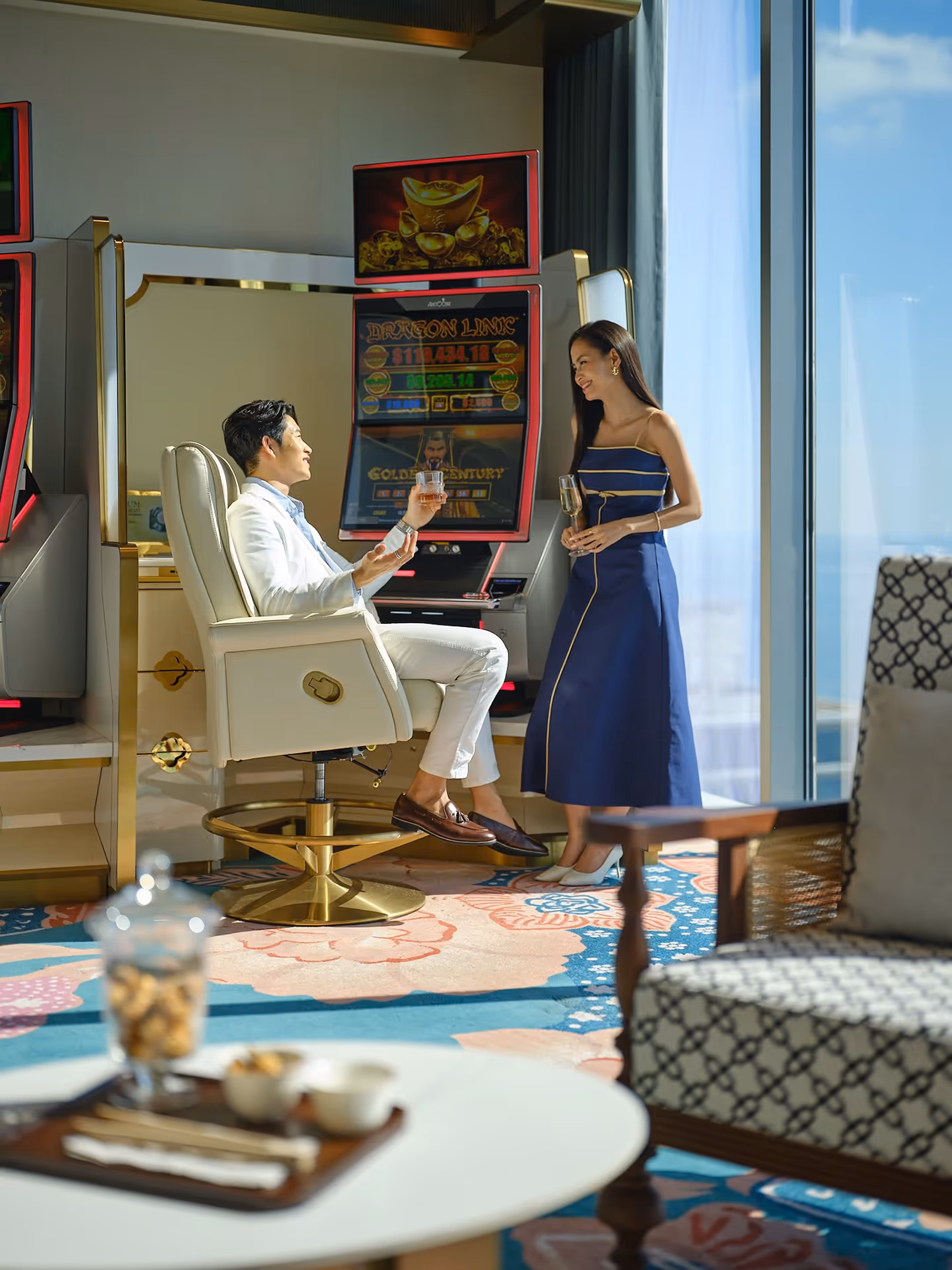 A Sky Casino host serving drinks to a guest seated at a slot machine at Hoiana Resort & Golf.
