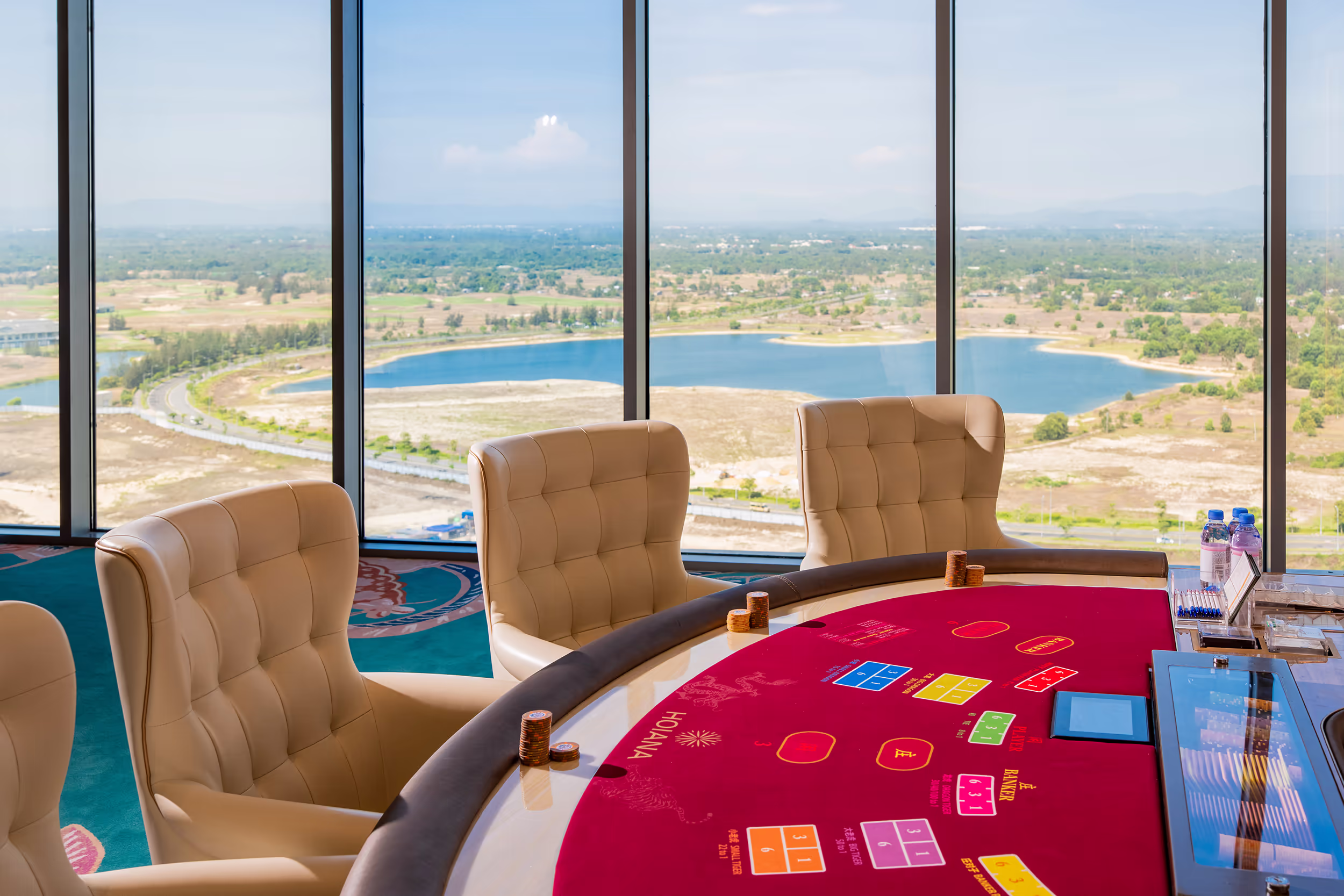 Baccarat table in a private Sky Casino room overlooking the lagoon and coastal landscape surrounding Hoiana Resort & Golf.
