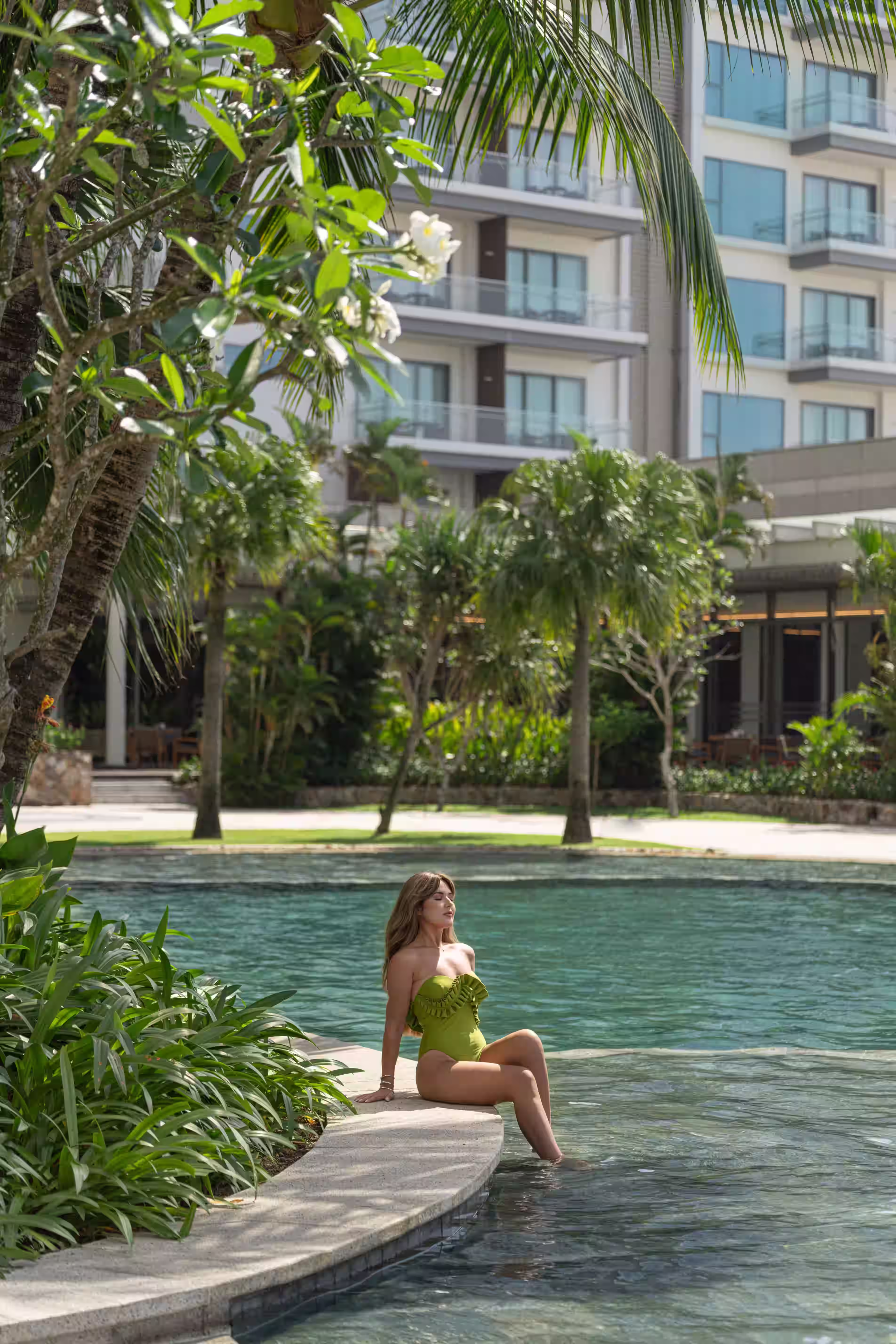 A guest relaxing at the edge of the tropical pool at New World Hoiana Hotel, surrounded by lush greenery.