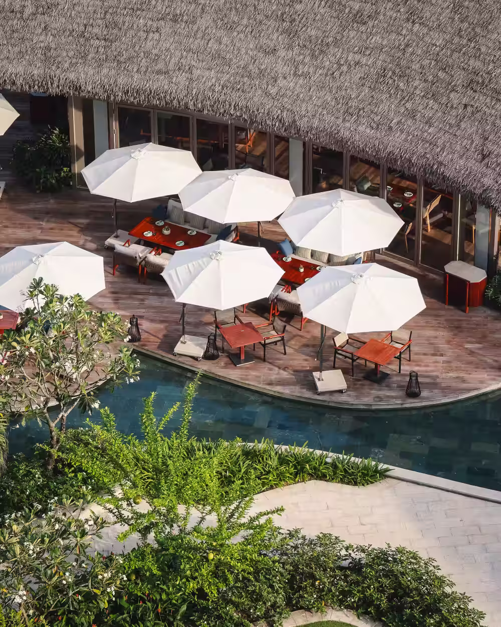 Elevated view of Charred restaurant’s relaxed poolside terrace at Hoiana Residences, with shaded tables, timber decking and tropical greenery.