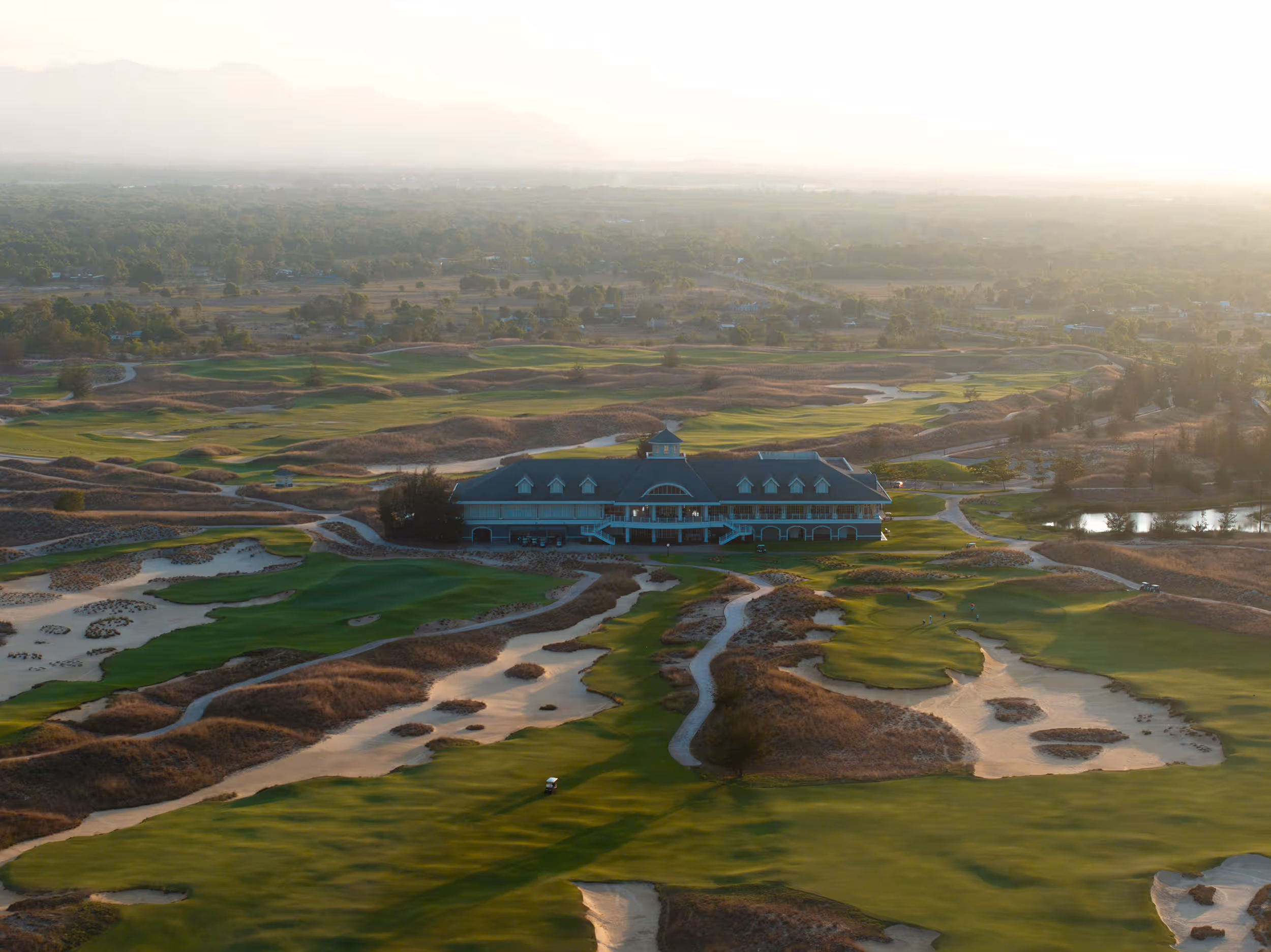 Golden-hour aerial view of the Hoiana Shores Golf Club clubhouse surrounded by fairways and sand dunes.