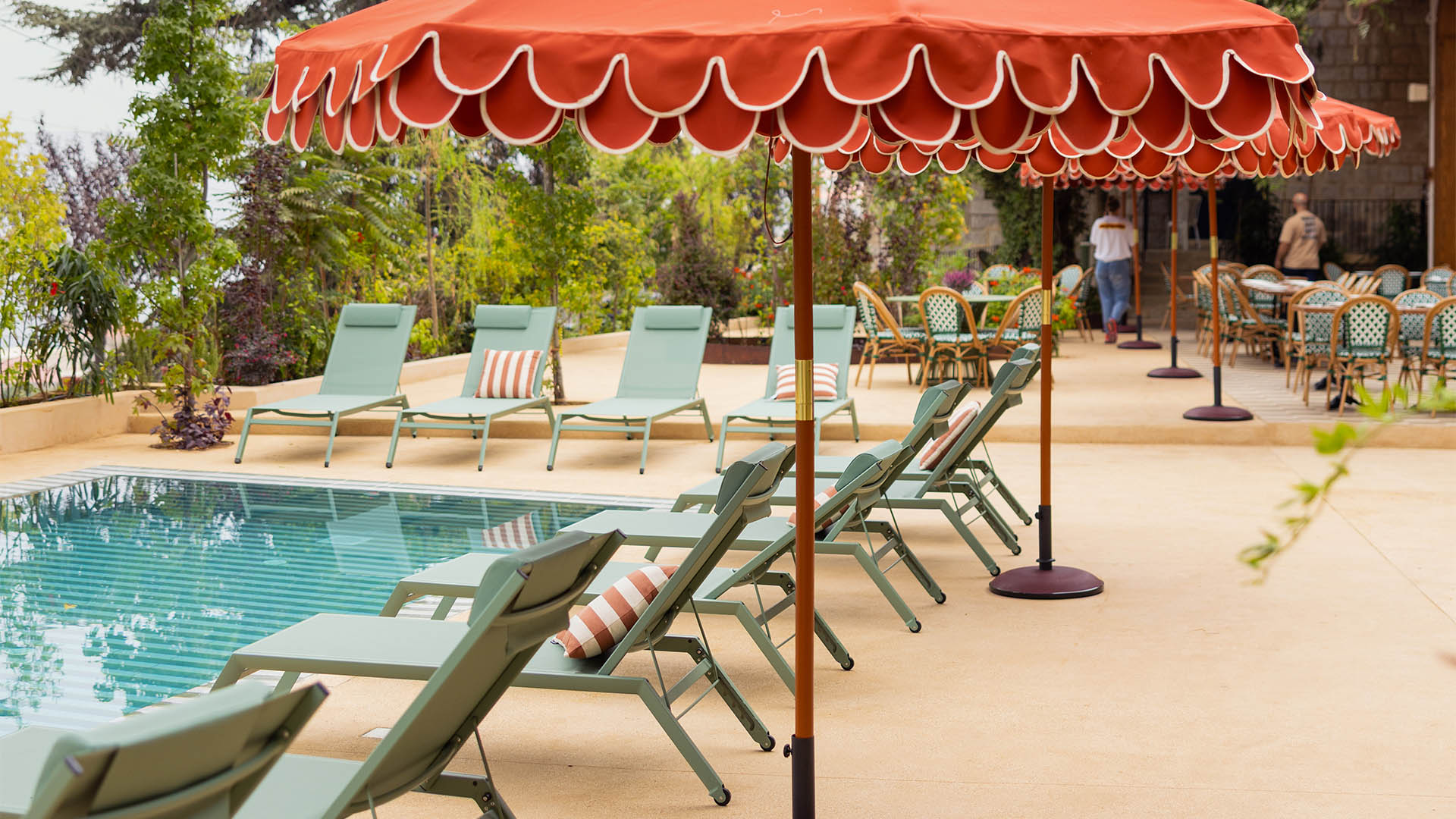Outdoor dining terrace at guesthouse with rattan chairs, patterned cushions, and red parasols