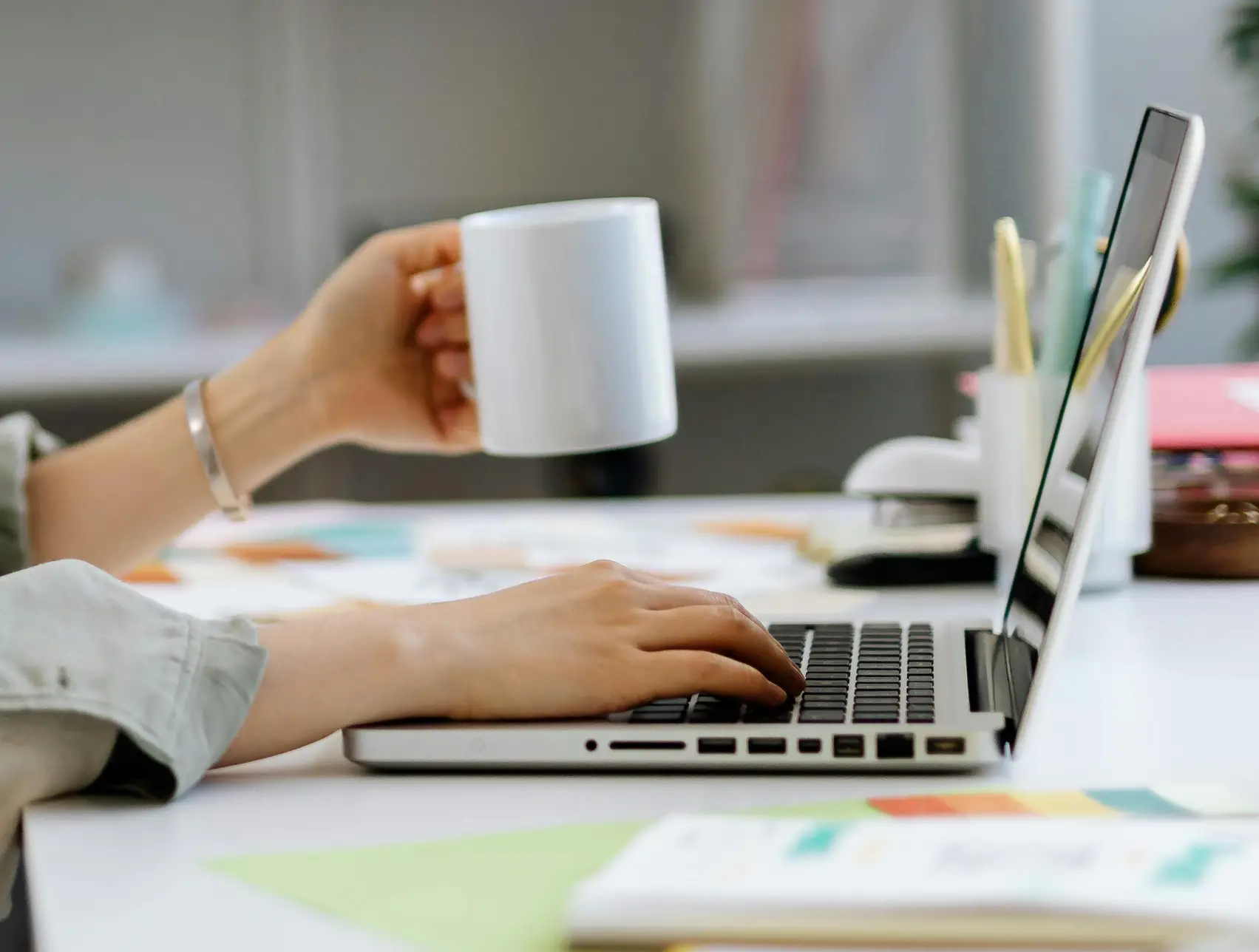 Hand holding a mug and another hand typing