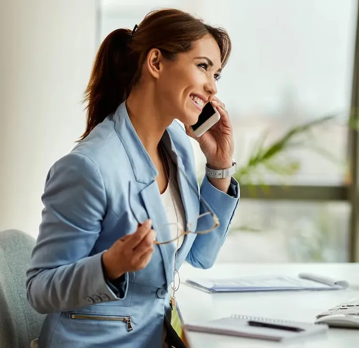 Smiling businesswoman talking on a mobile phone in an office setting.