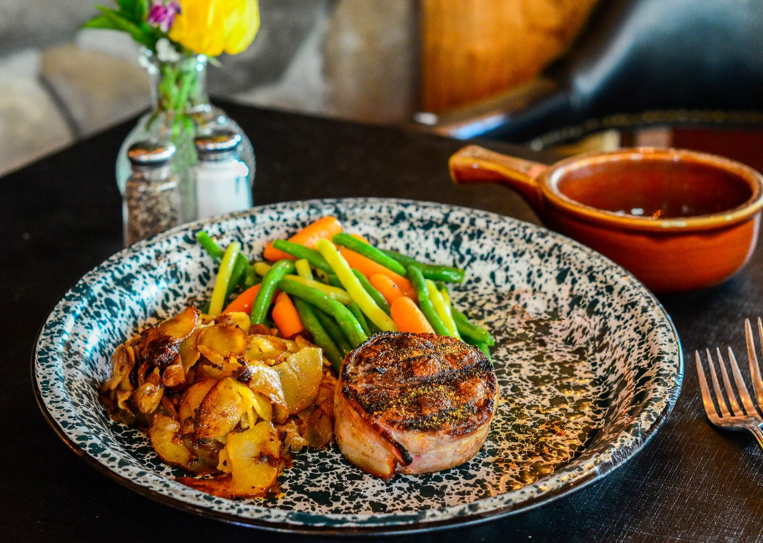 A plate featuring a grilled beef fillet, crispy sliced potatoes, and a side of vibrant green beans and carrots.