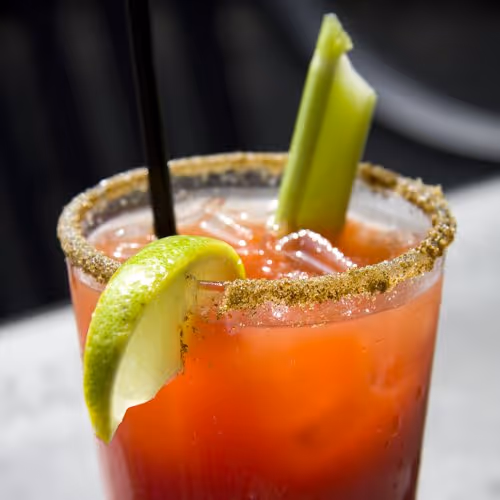 A close-up of a bloody mary with a salted rim, garnished with a lime wedge and celery stalk, ready to be enjoyed.