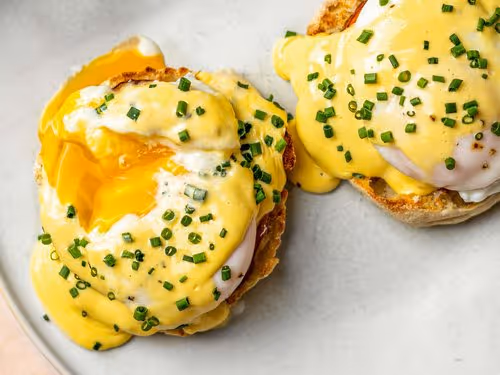 A plate of eggs benedict topped with chives, featuring poached eggs on English muffins and drizzled with hollandaise sauce.