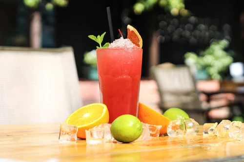 A glass of red drink with a lemon wedge and lime slice on the table.