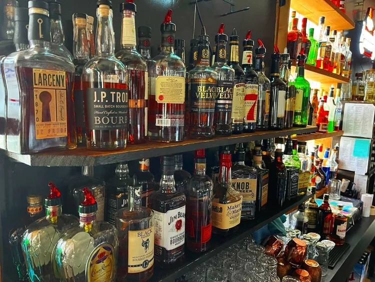 A shelf full of liquor bottles including Black Jack whiskey.