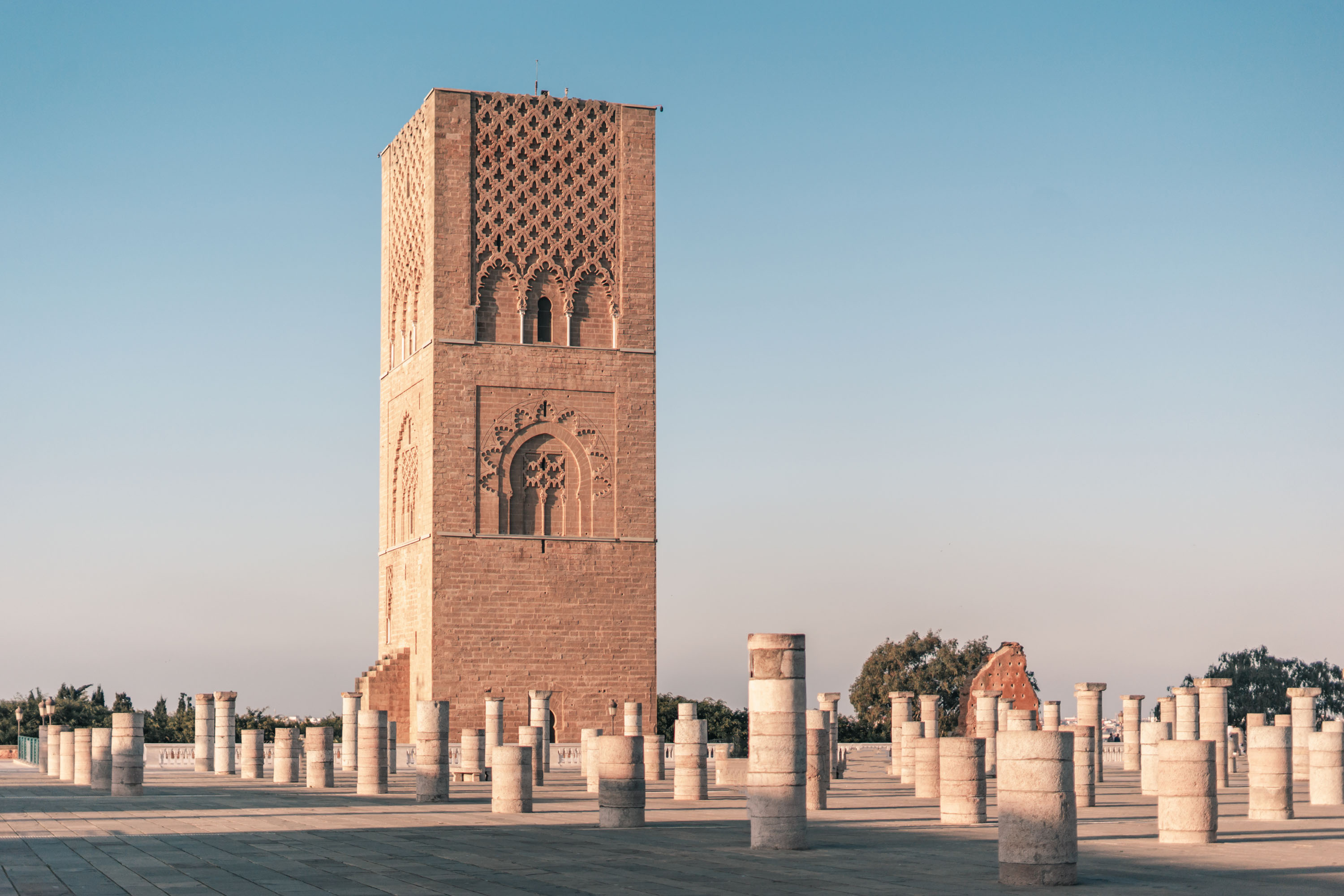 Tall sandstone Hassan tower in Morocco Rabat with ornate geometric carvings surrounded by numerous short stone columns under a clear blue sky during a guided trip with Moroccan guides travel.