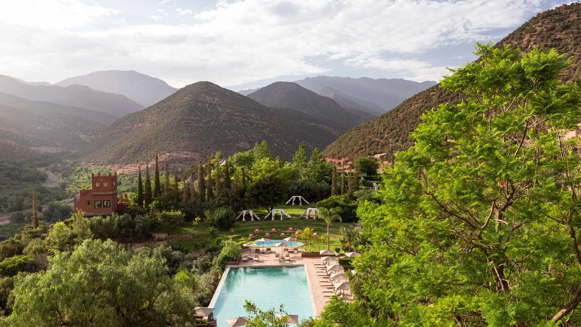 Outdoor pool area with lounge chairs and umbrellas set in a lush garden surrounded by green hills in the atlas mountains of morocco