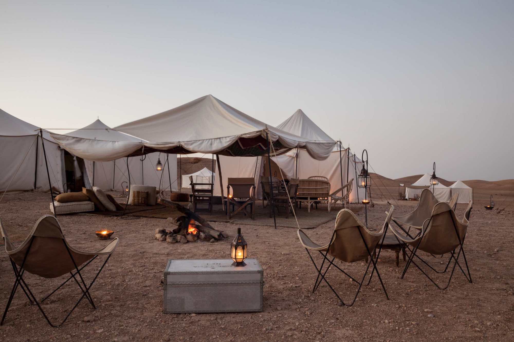 Evening view of a comfortable, fire-lit seating area inside a luxury tent at a Moroccan Agafay desert camp.