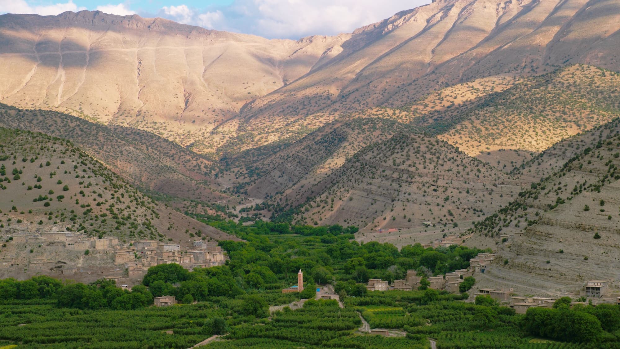 A mountain village nestled in lush green Ait Bougemez Happy Valley with rocky high atlas peaks in Morocco